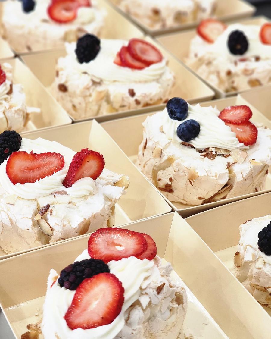 Individual almond pavlova bites topped with fresh strawberries, blackberries and blueberries in takeout boxes
